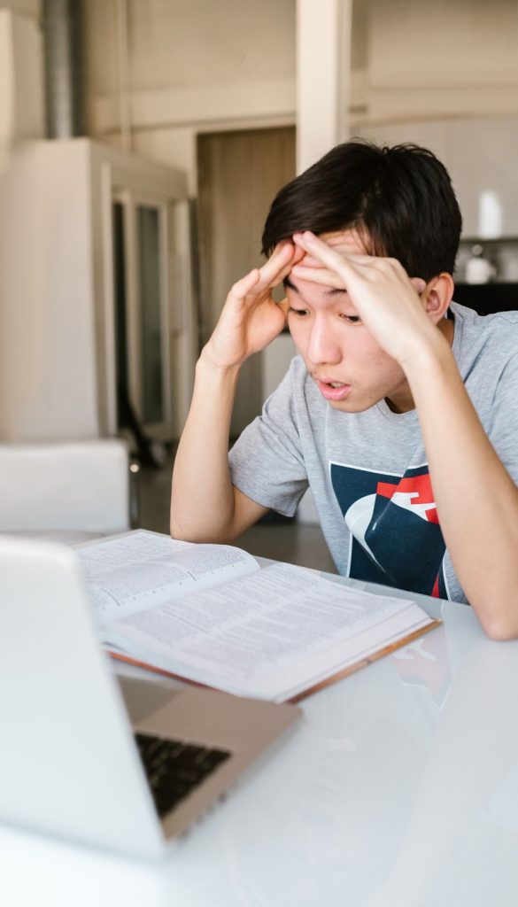 An older teenage student revising from an open textbook beside a laptop