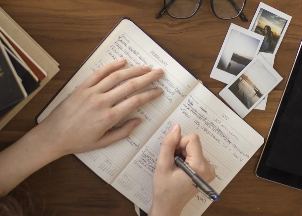 A hand writing in an open notebook on a wooden table