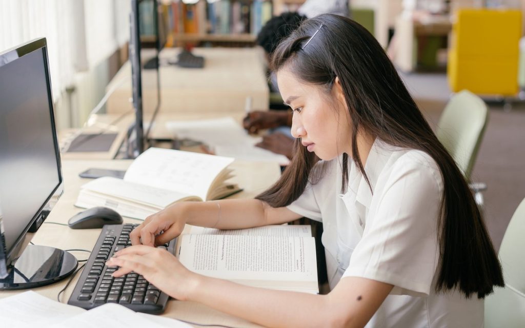 A teenage student studying from an open book in a library